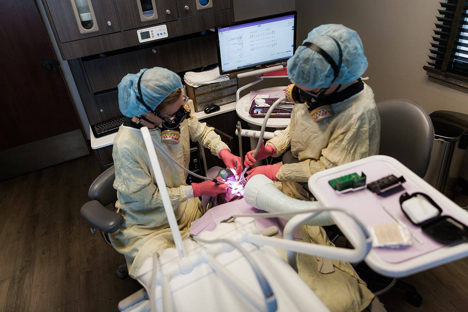 In our Tulsa, Oklahoma dental practice, two holistic and health-centered dentists, clad in protective gear, diligently perform a procedure within a state-of-the-art environment. Surrounded by cutting-edge equipment designed to support optimal oral health and wellness, they are guided by the information displayed on a nearby computer screen. This vital data underscores their dedication to providing comprehensive and integrative dental care that prioritizes patients' overall well-being.
